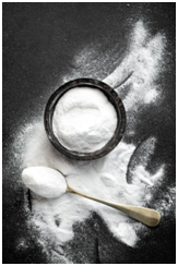 A top view of baking soda in a bowl, spoon, and some sprinkled around