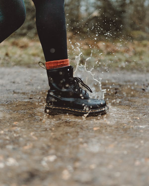 Water splashing from a person in black boots stepping on wet pavement